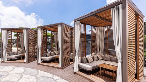 Varias cabañas de madera con asientos acolchados y cortinas, ubicadas sobre una terraza con baldosas.