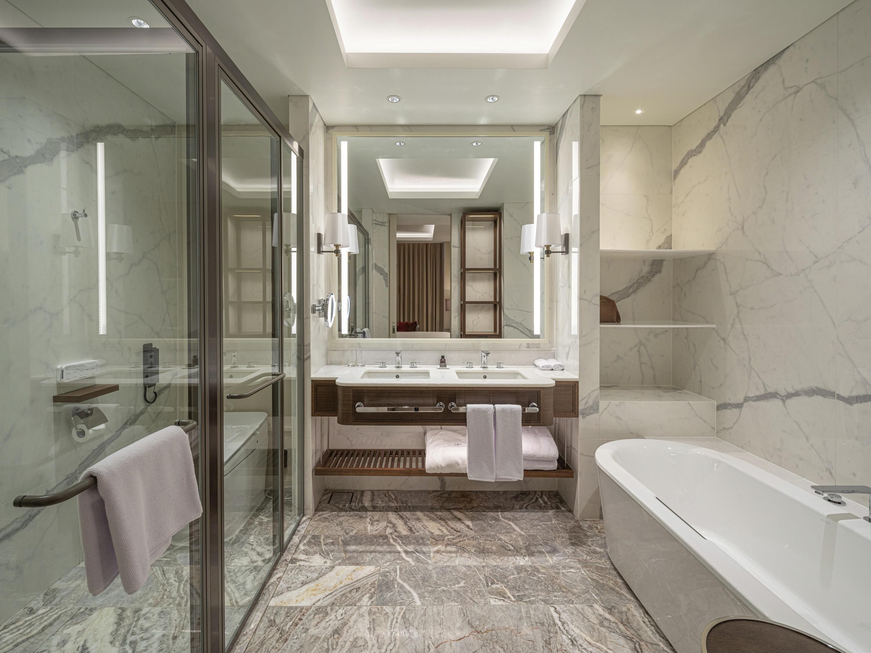 A modern bathroom with a glass-enclosed shower, a double sink vanity, a large mirror, and a freestanding bathtub.