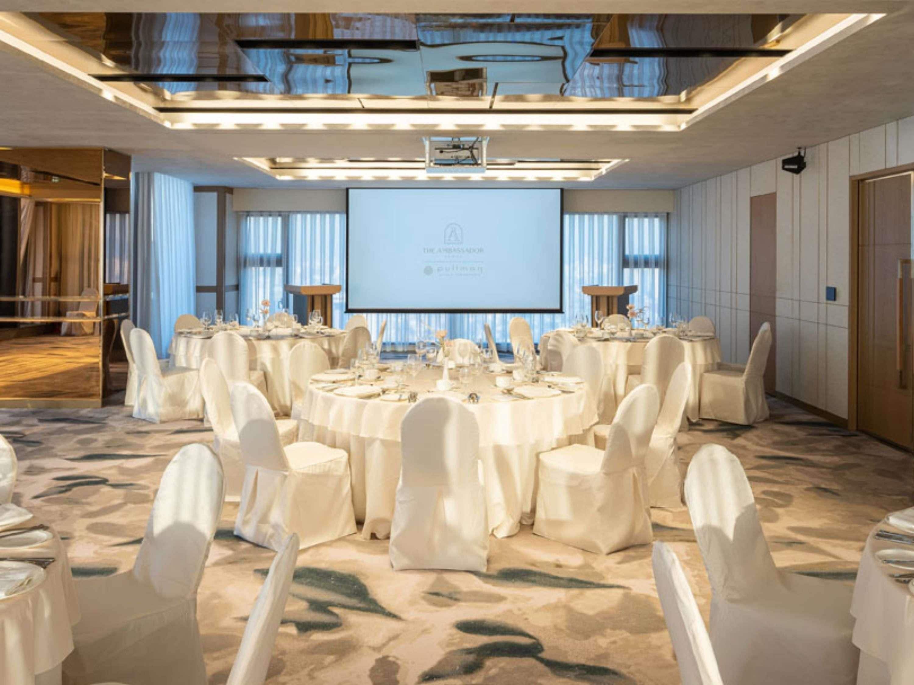 A conference room with round tables, white chairs, a large screen, and a modern ceiling design.