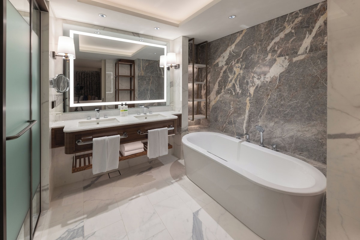 A modern bathroom with a freestanding bathtub, a large mirror, and marble walls.