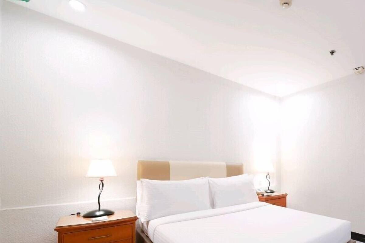 A hotel room with a large bed, two bedside tables with lamps, and a ceiling light.