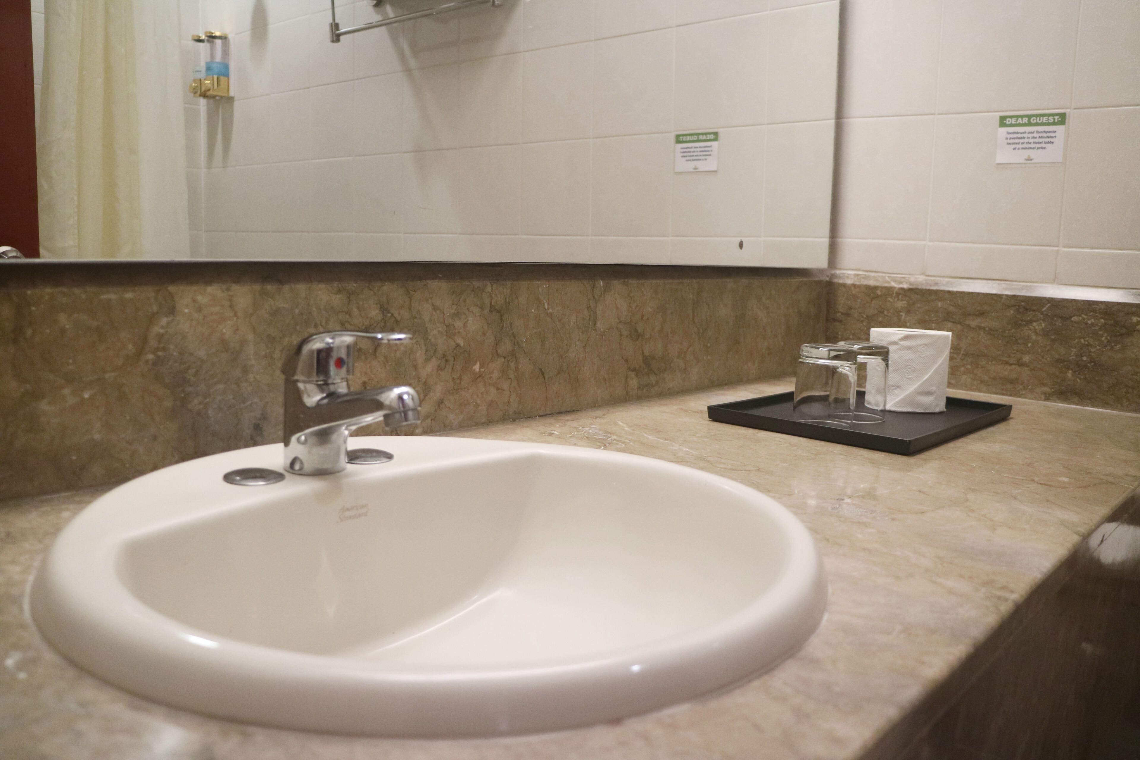 A bathroom sink with a marble countertop, a mirror, and a "Dear Guest" sign.