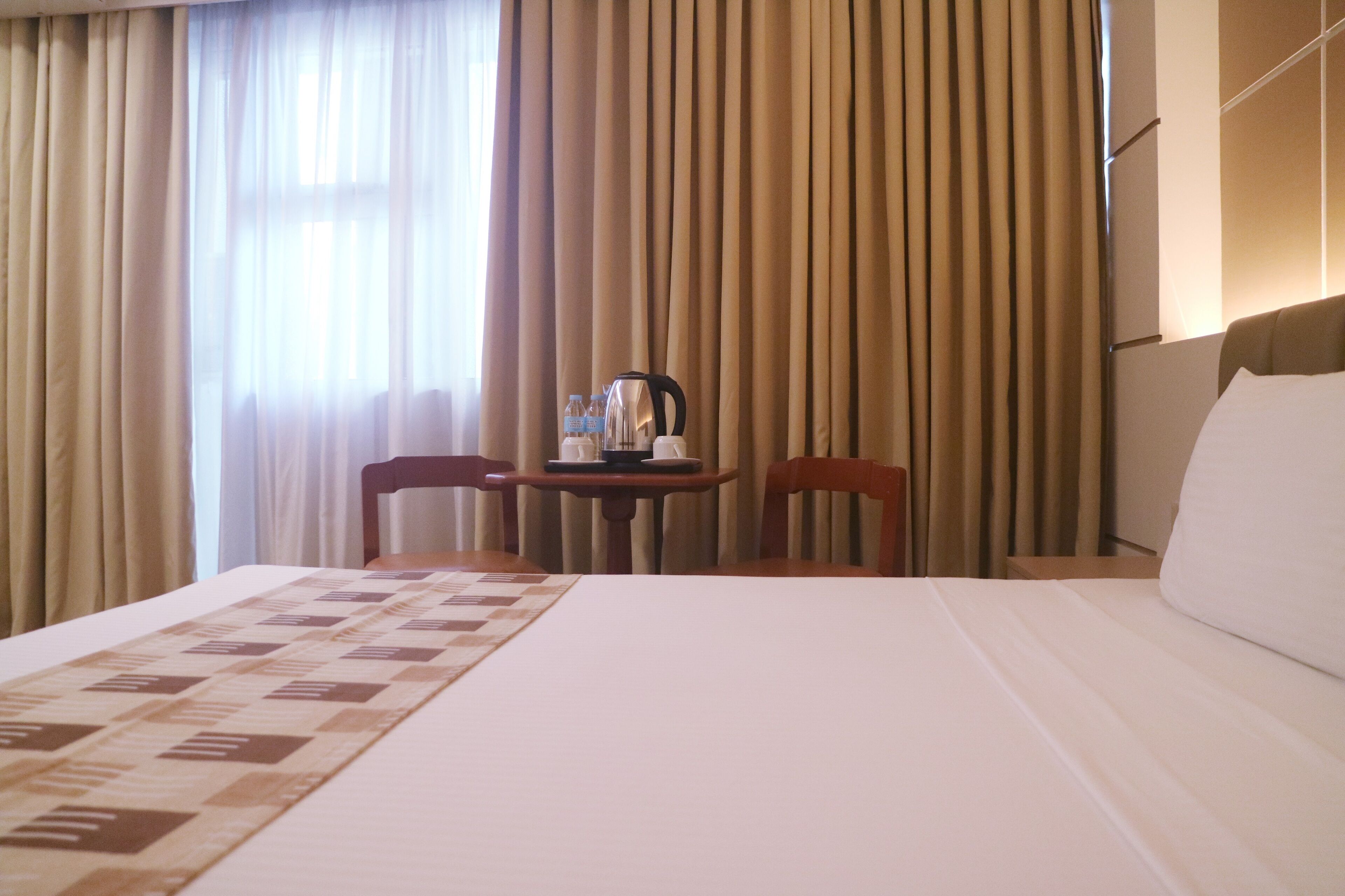 A hotel room with a large bed, a table with a kettle, two chairs, and curtains.