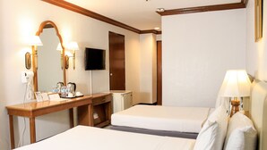 Une chambre d’hôtel avec deux lits, un bureau avec un miroir, une télévision et une lampe.