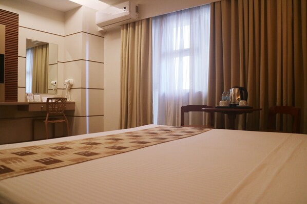 Habitación de hotel con una cama grande, un escritorio con una silla, un espejo, un secador de pelo y una cafetera.