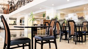 Un espace intérieur spacieux comprenant plusieurs tables et chaises, une rambarde décorative et des plantes en pot.