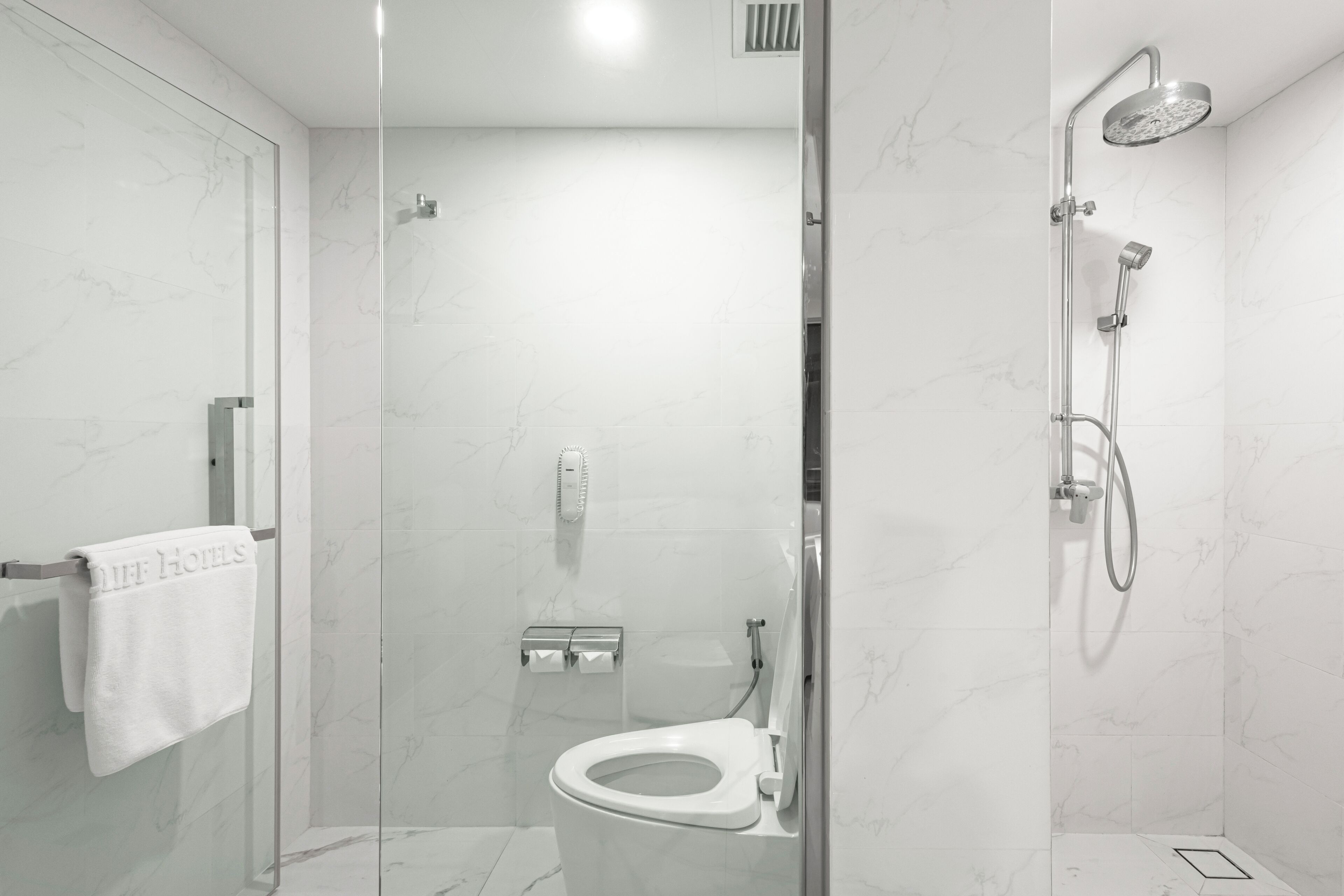 A modern bathroom with a glass-enclosed shower, a toilet, and a towel rack with a towel.