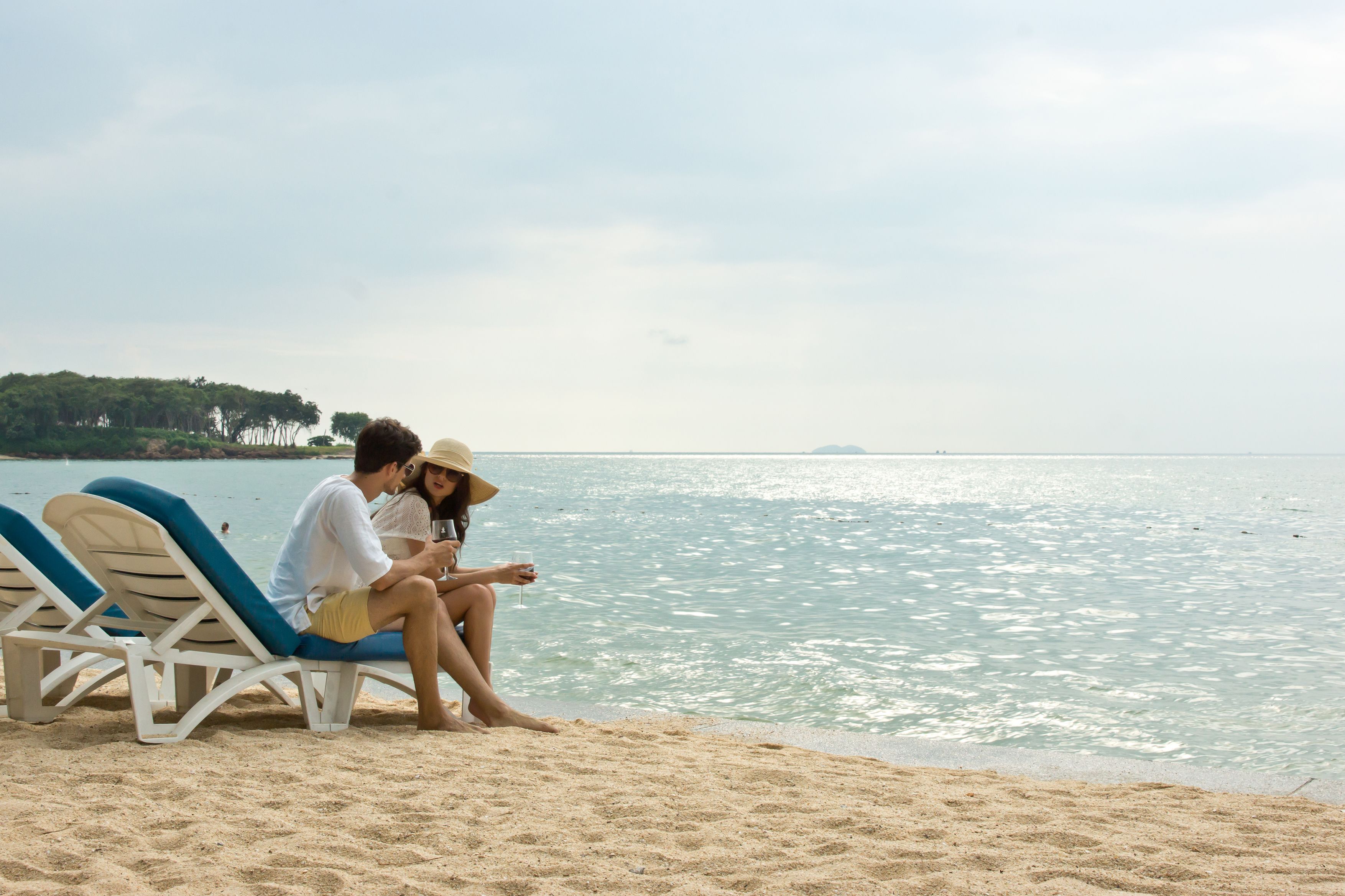 A couple sitting on beach chairs by the sea, with a sandy beach and calm waters in the background.