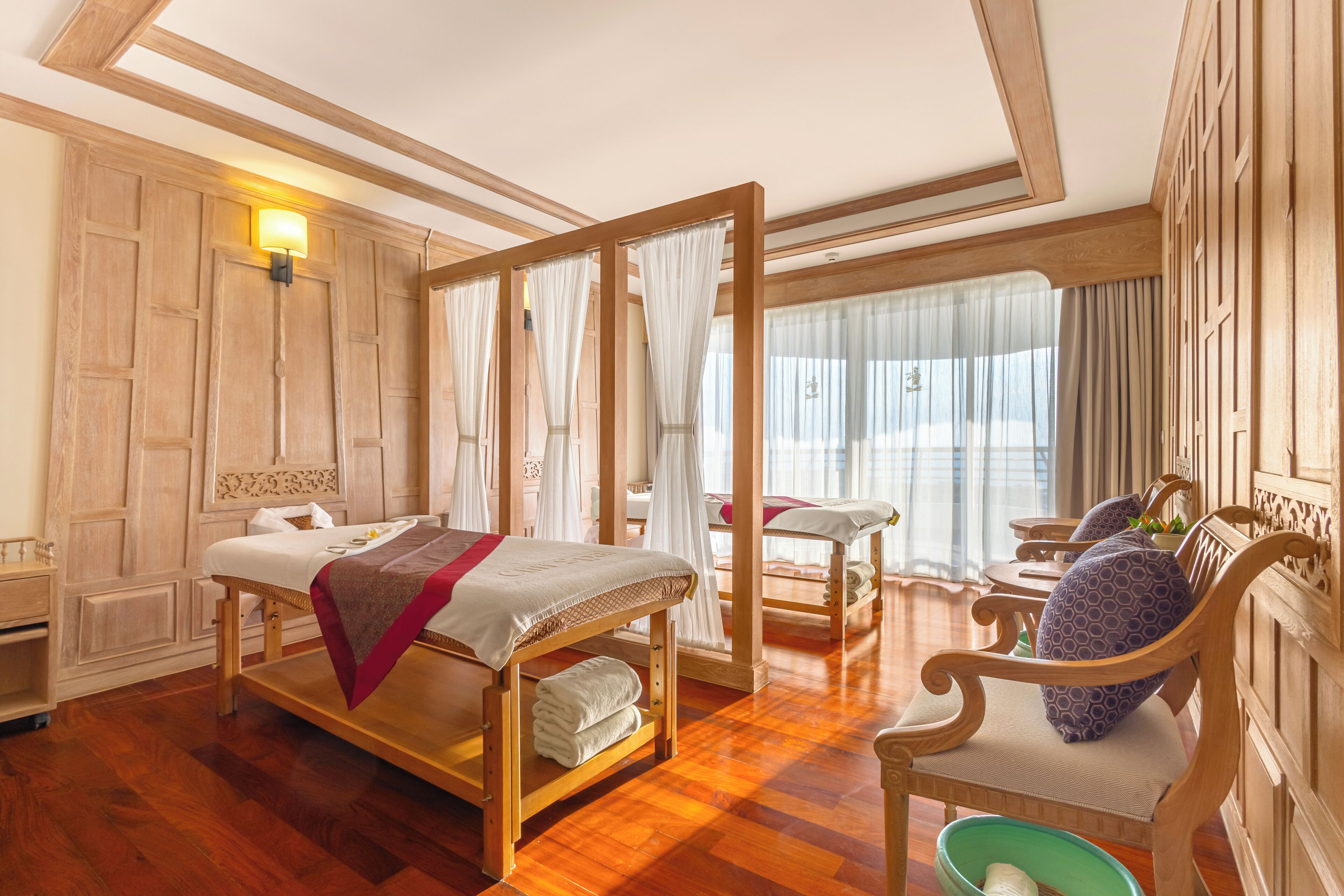 A hotel room with a wooden bed, a wooden chair, a small table, and a window with curtains.