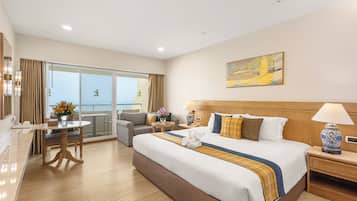 A hotel room with a large bed, a sitting area with a table and chairs, a balcony with a view, and a painting on the wall.