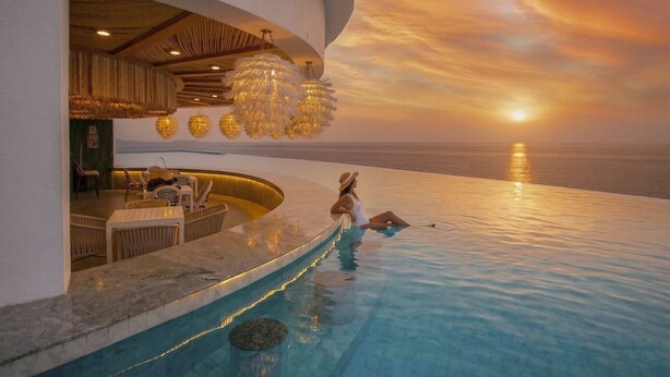 Zona de piscina con vista al atardecer, un bar y mobiliario exterior.