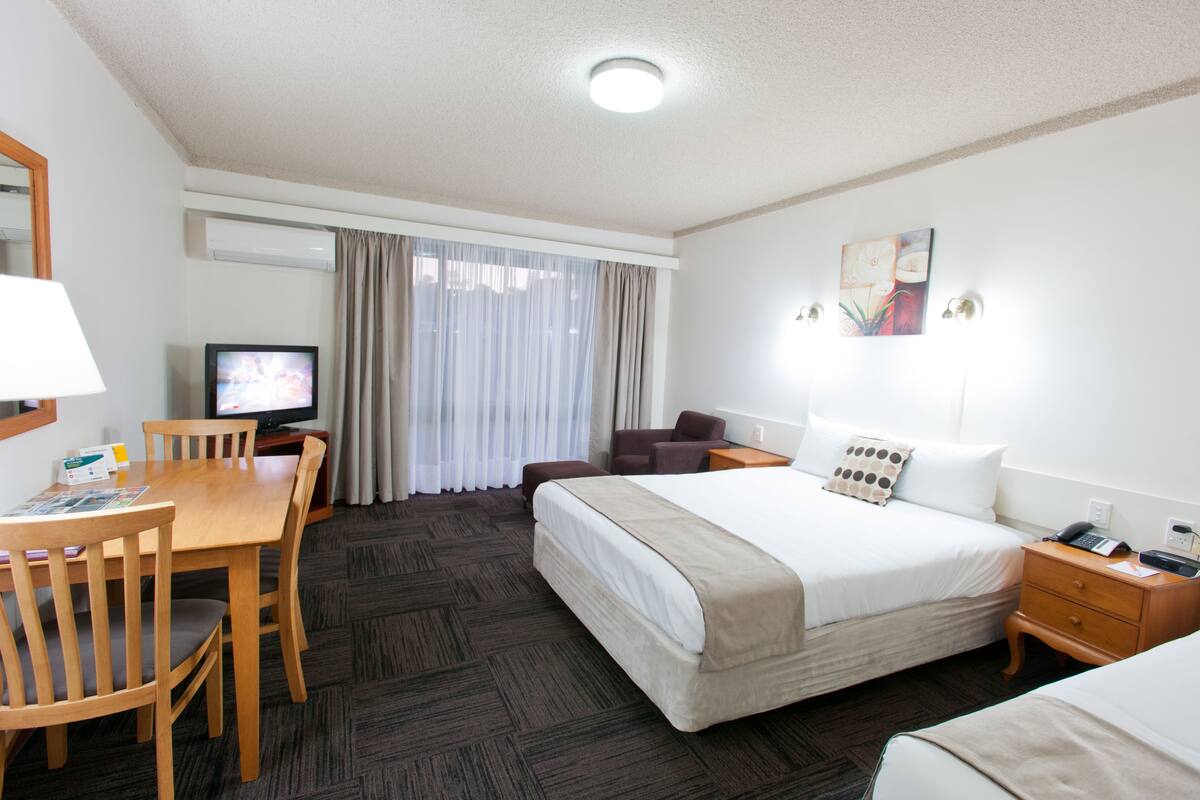 Habitación de hotel con cama, escritorio con silla, televisor y ventana con cortinas.
