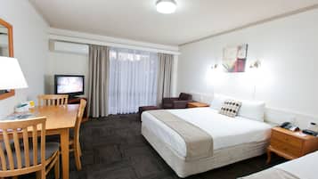 Quarto de hotel com uma cama, uma escrivaninha com cadeira, televisão e uma janela com cortinas.
