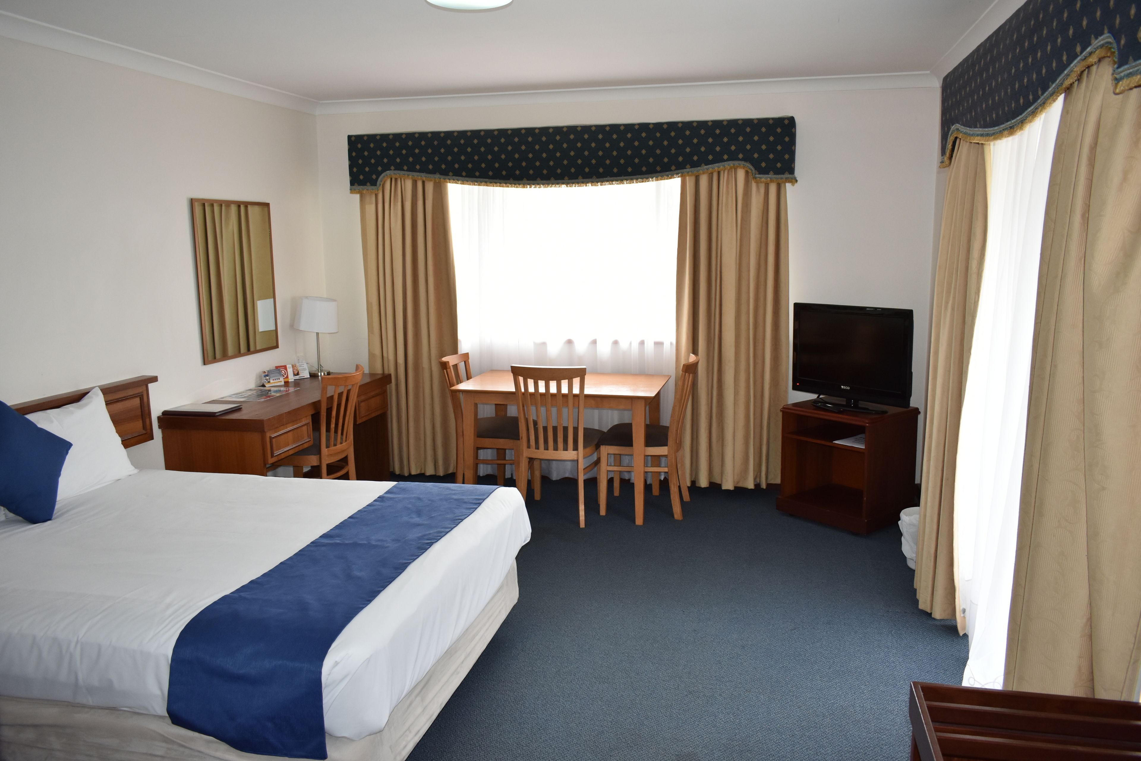 A hotel room with a bed, desk, chairs, television, and curtains.