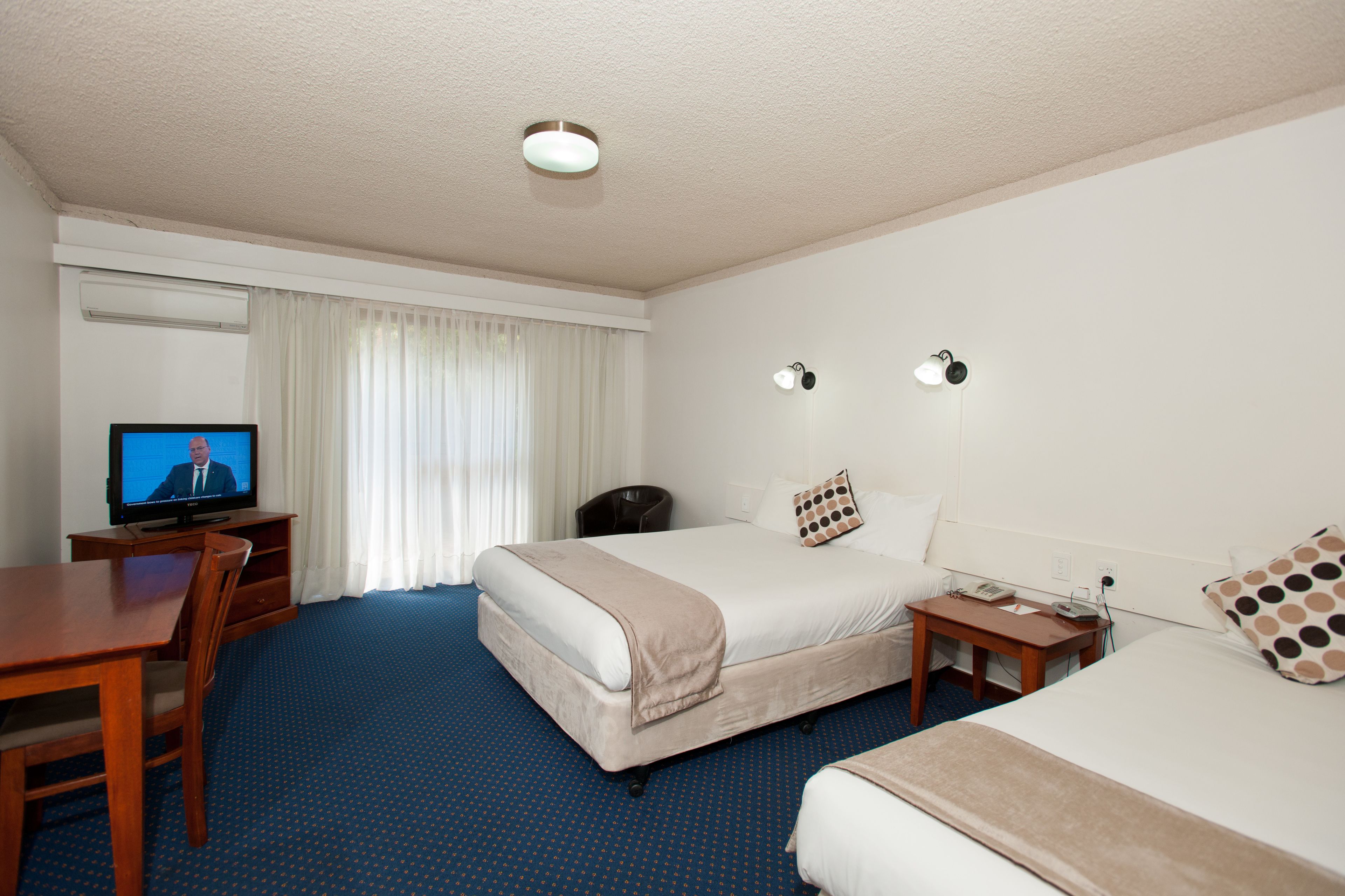 Een hotelkamer met een groot bed, een kleiner bed, een bureau met een televisie en een stoel.