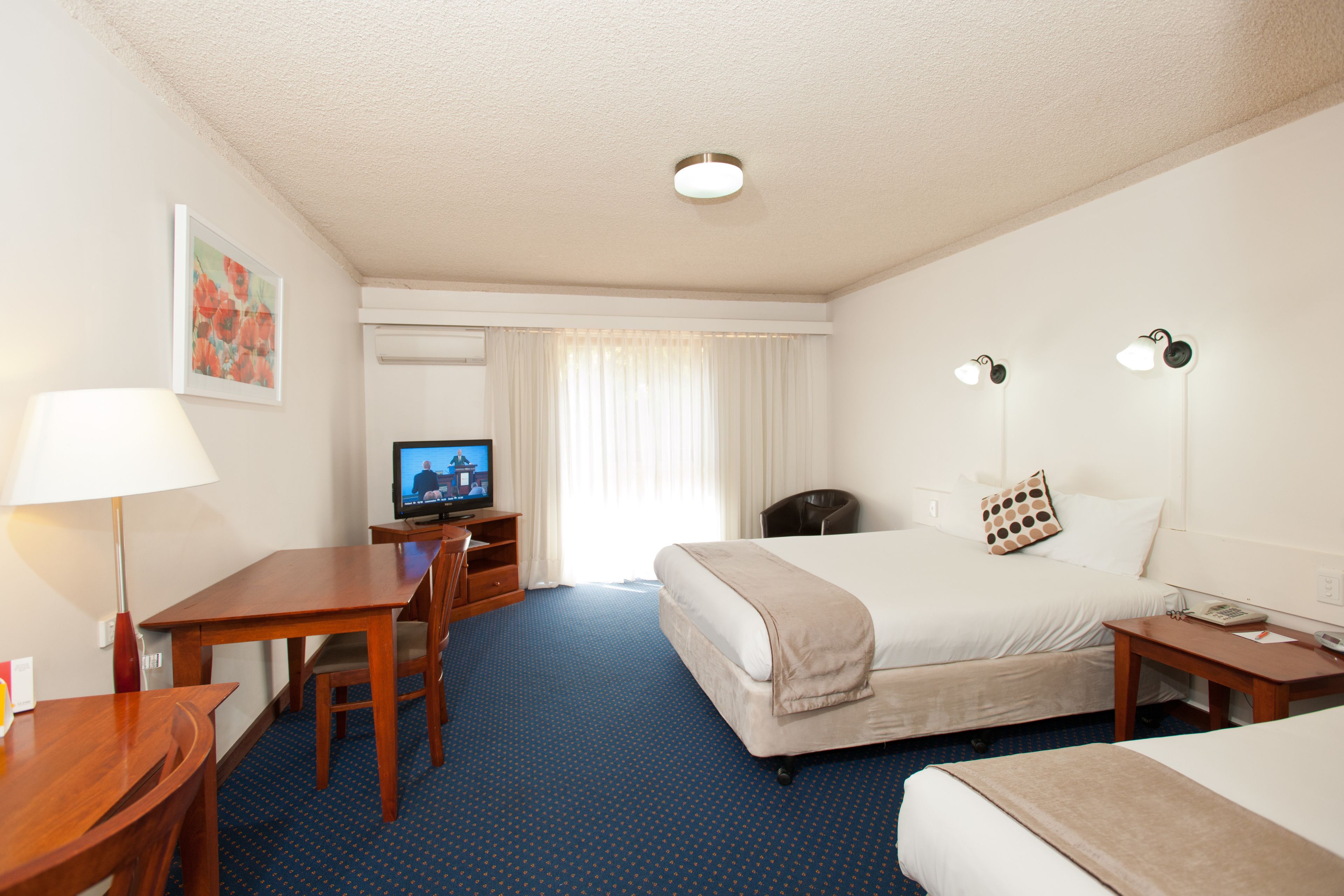 A hotel room with a bed, a desk, a chair, a television, and a lamp.