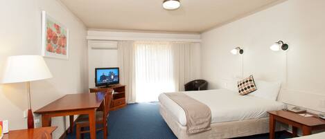A hotel room with a bed, a desk, a chair, a television, and a lamp.