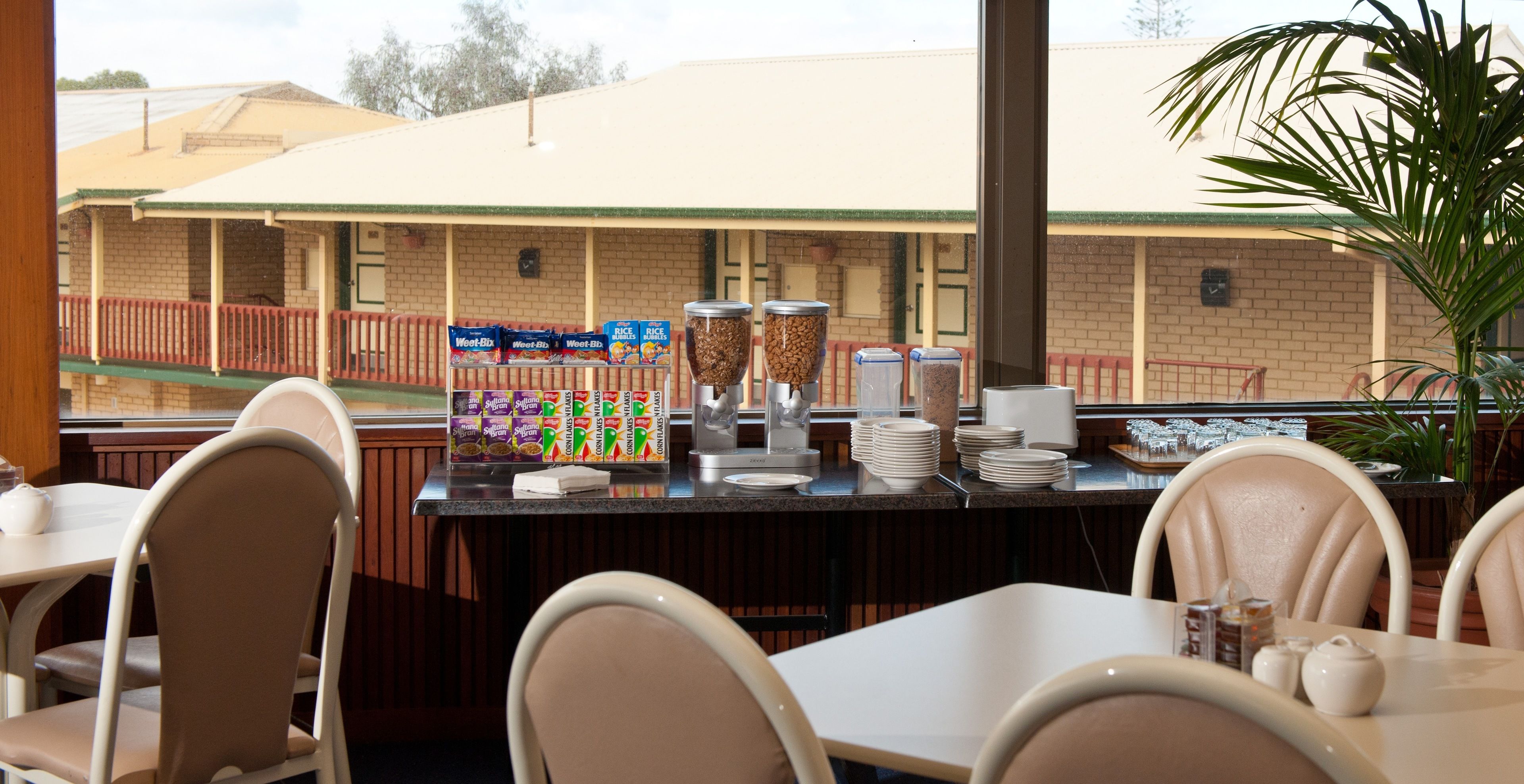 A breakfast bar with cereal boxes, coffee dispensers, and stacked plates.