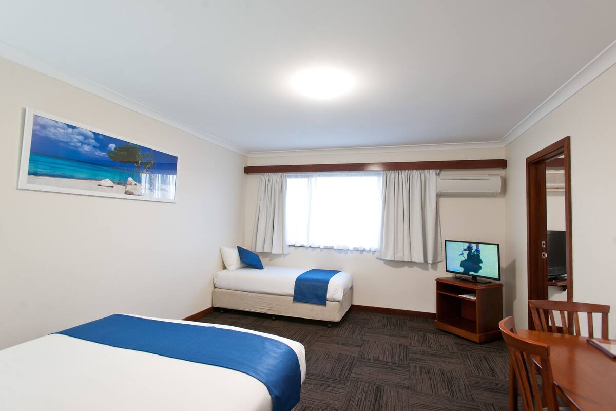 Habitación de hotel con dos camas, un televisor, una mesa de comedor y un cuadro con una playa.
