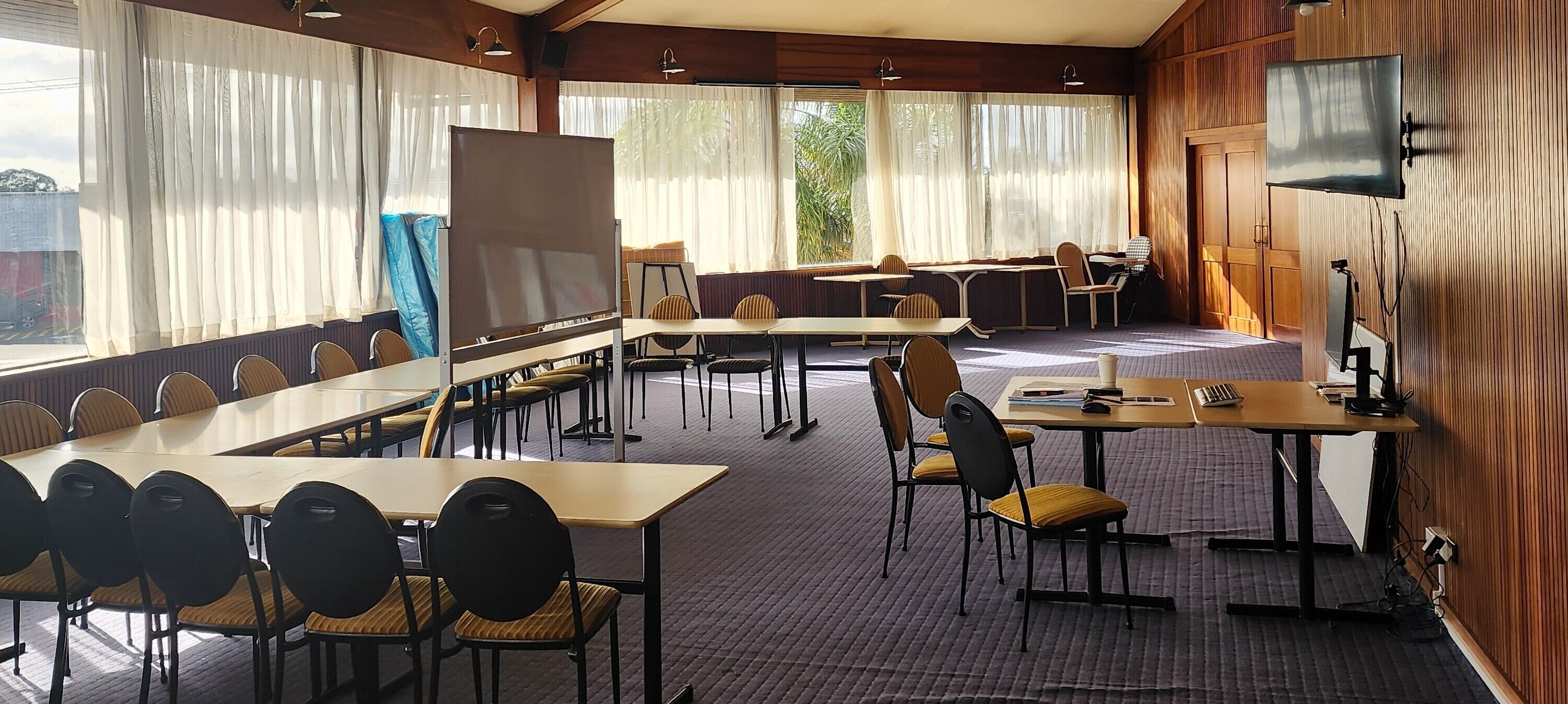Una sala de conferencias con mesas, sillas, una pantalla de proyección y una televisión.