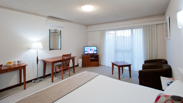 Quarto de hotel com cama, escrivaninha, cadeira, televisão e janela com cortinas.
