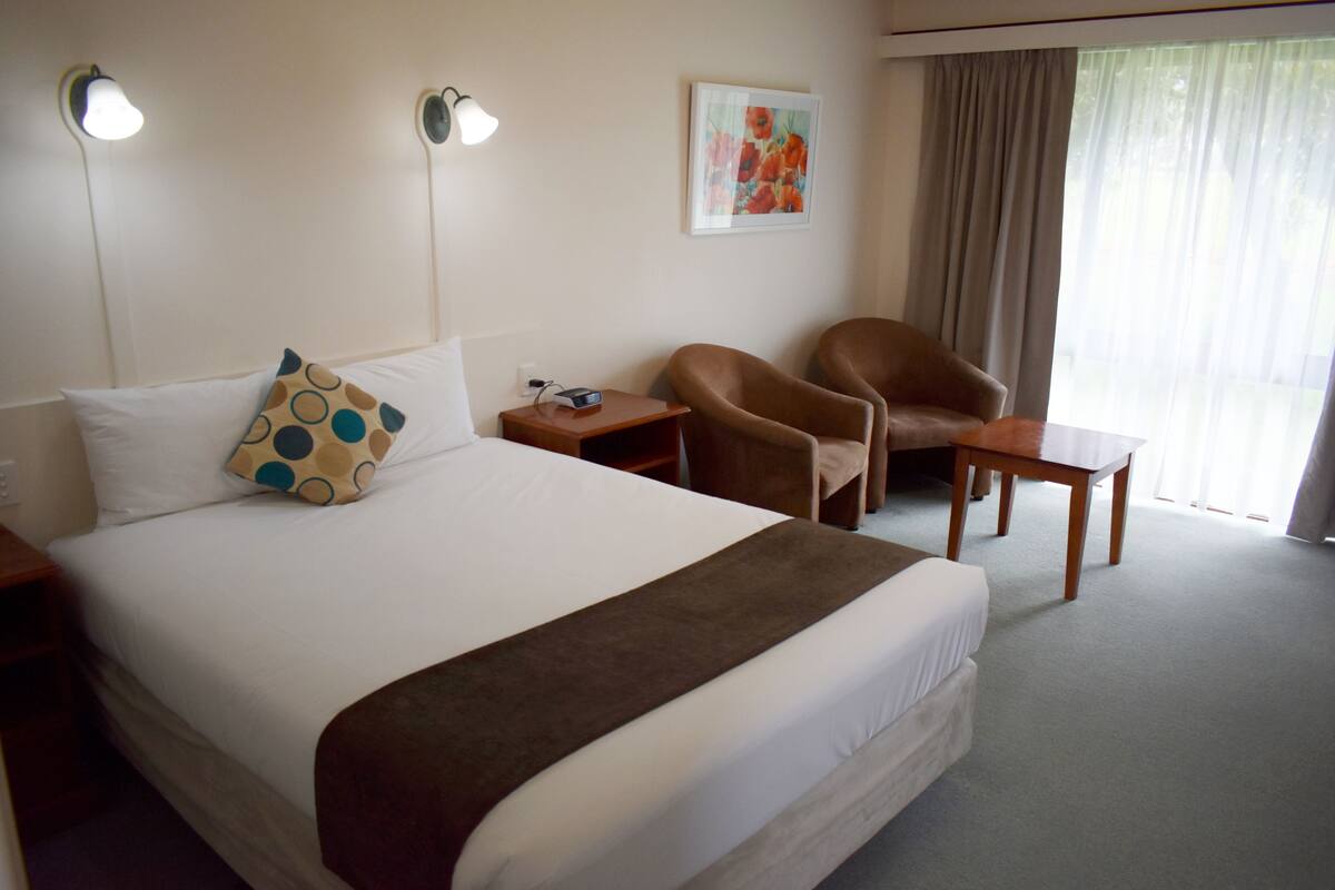 Habitación de hotel con una cama grande, un escritorio, una silla y un cuadro en la pared.