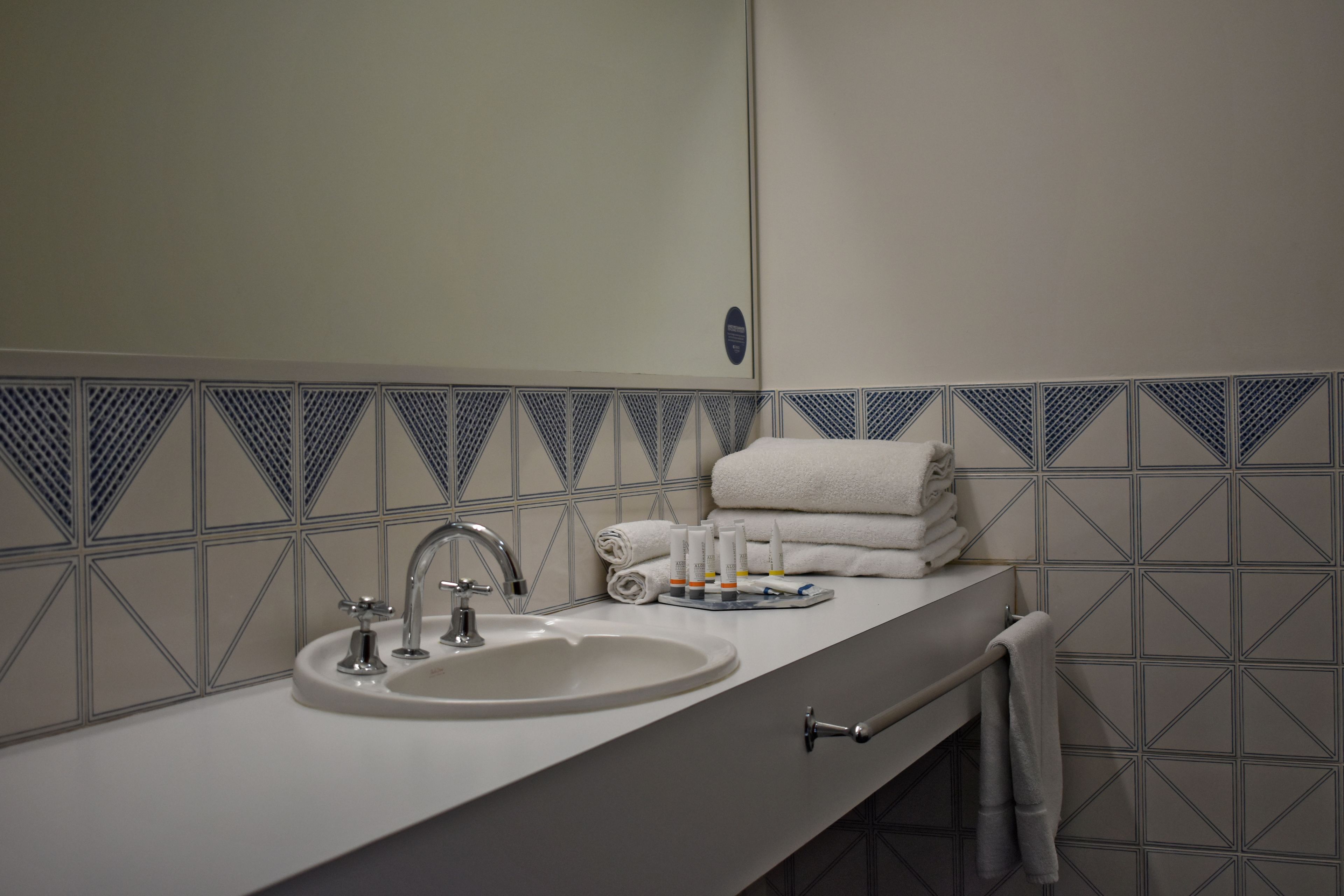 A bathroom with a sink, mirror, towel rack, and toiletries.
