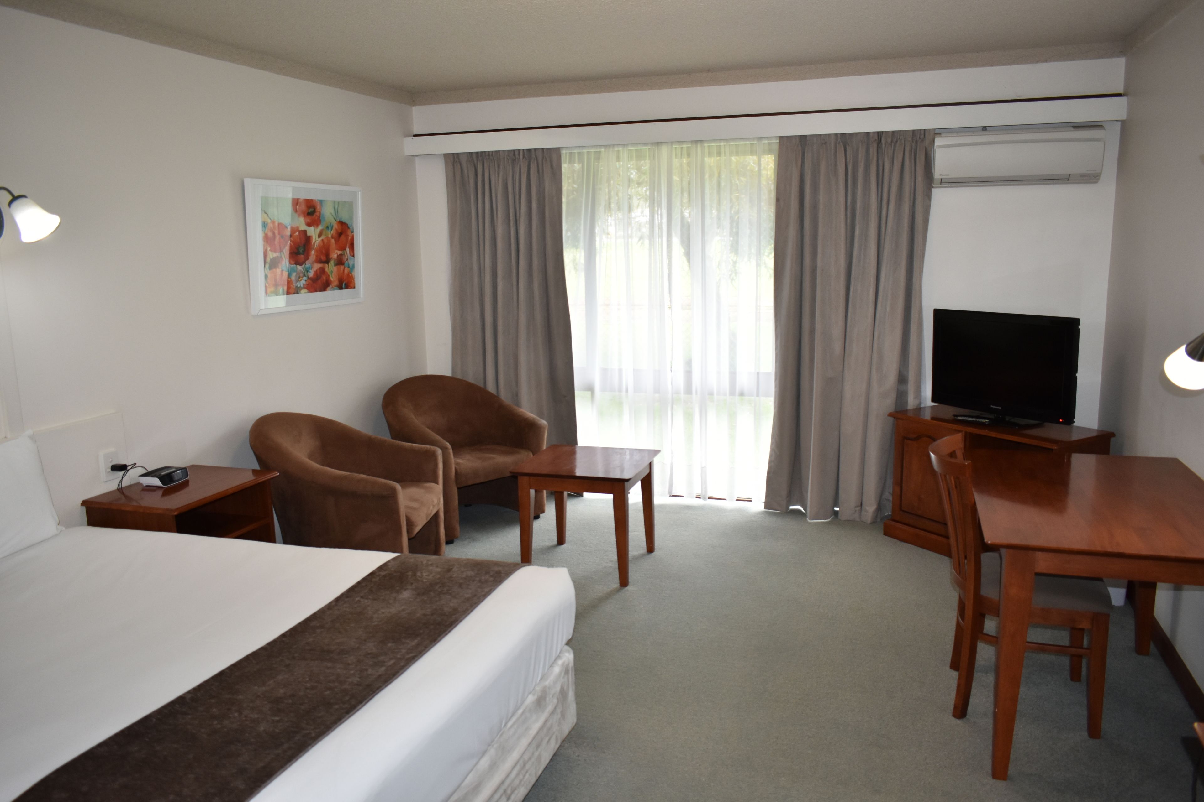 Habitación de hotel con cama, escritorio, silla, televisor y un cuadro en la pared.