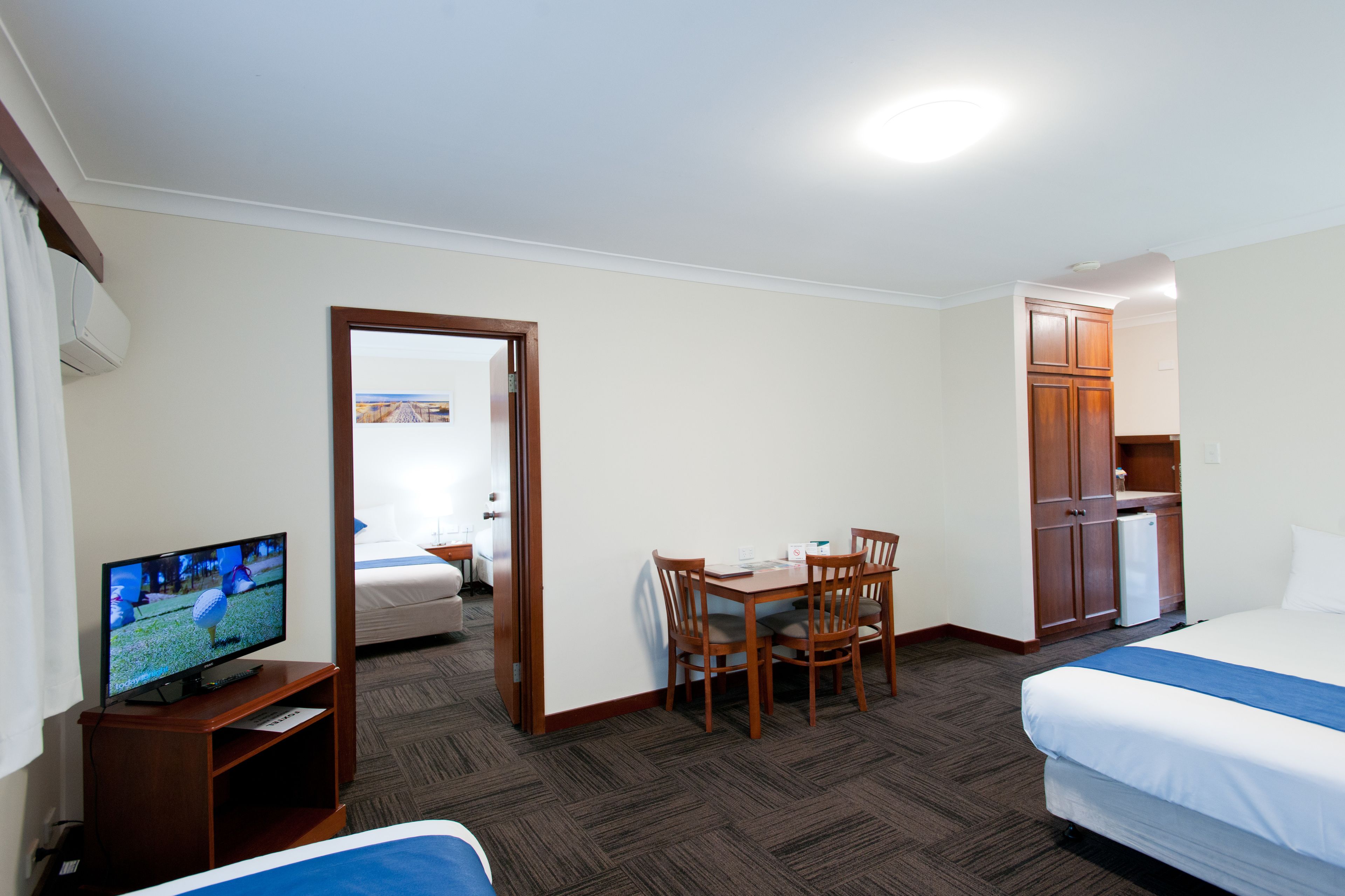 A hotel room with a bed, a TV on a stand, a dining table with chairs, and a small kitchenette.