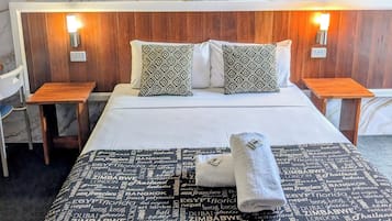 Habitación de hotel con pared de diseño de mármol, cama bien hecha con almohadas estampadas, dos mesitas de noche y una lámpara de pared.
