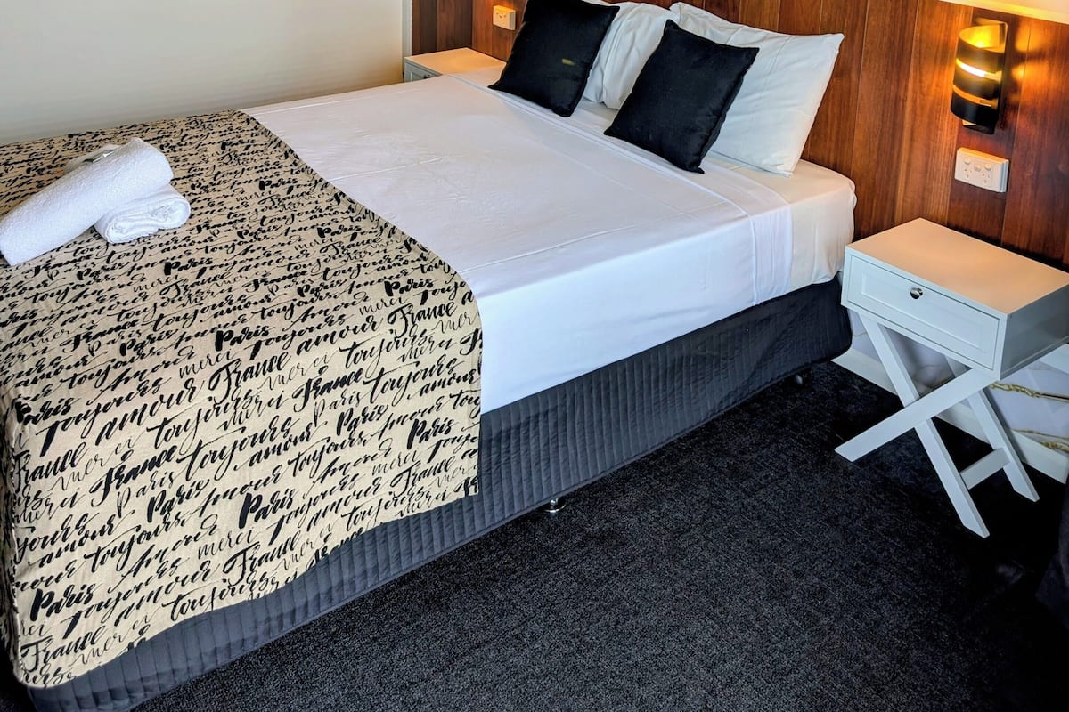 A hotel room with a bed, a nightstand, a wall-mounted light, and a framed picture.