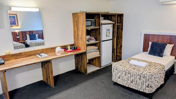 A hotel room with a bed, a desk with a mirror, a wardrobe, and a refrigerator.