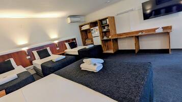 Ein Hotelzimmer mit drei Betten, einem flachbildfernseher an der Wand, einem Holztisch und einer eingebauten Mikrowelle.
