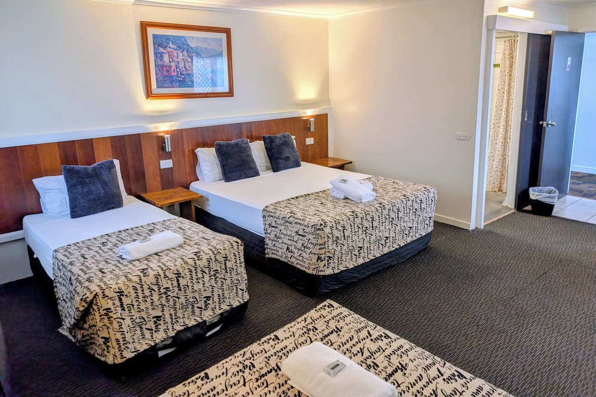 A hotel room with two beds, a wooden headboard, a framed picture on the wall, and a bathroom door visible.