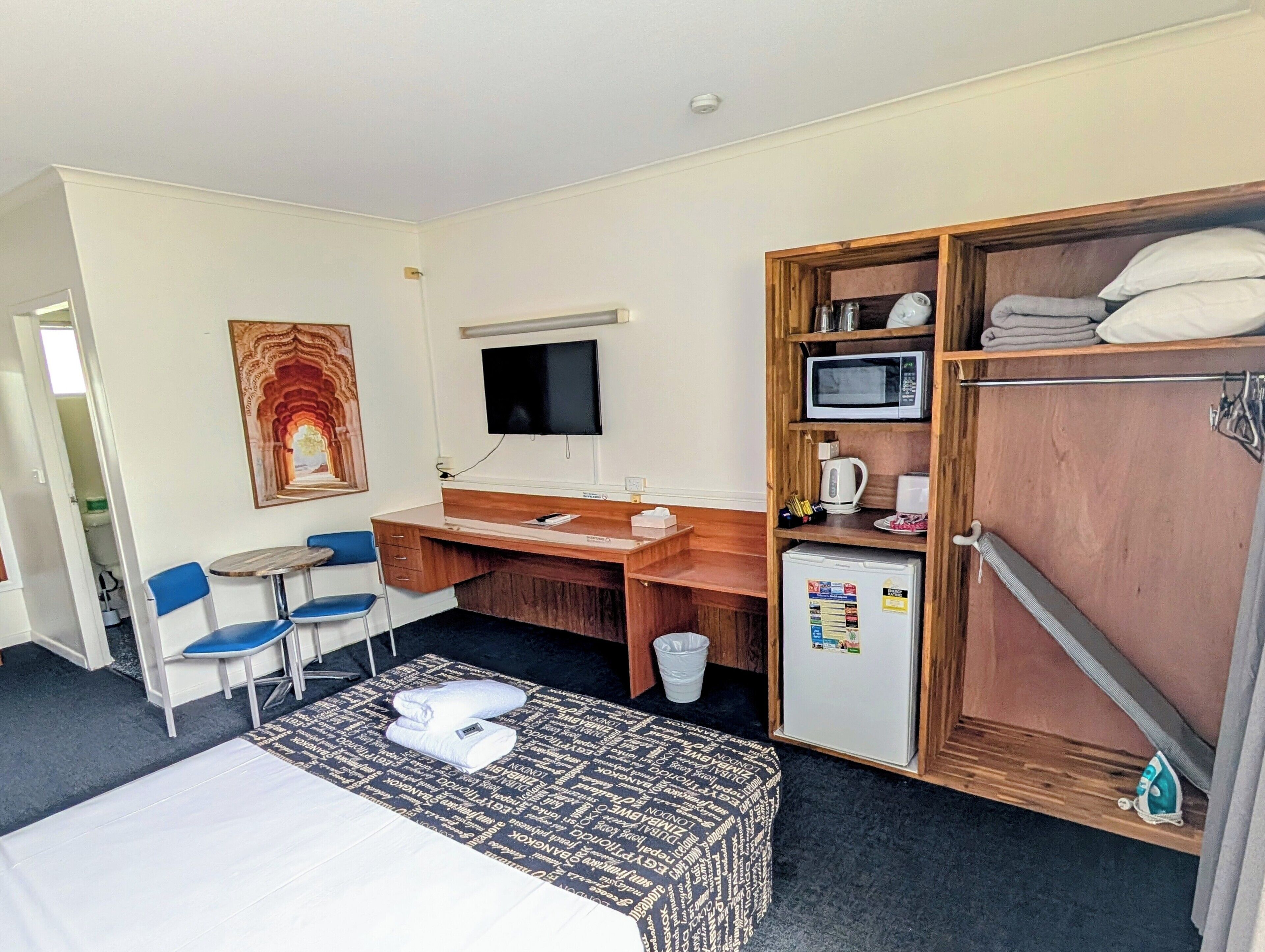 A hotel room with a bed, a desk with a computer, a chair, a TV, a microwave, and a wardrobe.