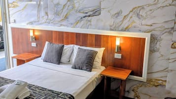 Una habitación de hotel con una cama grande, cabecera de madera, dos mesitas de noche y una pared con diseño de mármol.