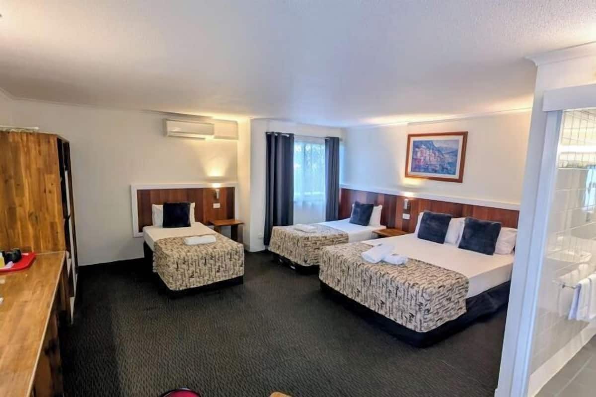 A hotel room with two beds, a wooden desk, a small table, and a window with curtains.