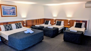 A hotel room with four beds arranged in a row, each with a pillow and a folded towel. There is a painting of a Mediterranean view on the wall. - Hampton Villa Motel (Rockhampton)