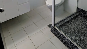 A modern bathroom with a glass shower enclosure, white tiles, a sink with a mirror, and a toilet. - Hampton Villa Motel (Rockhampton)