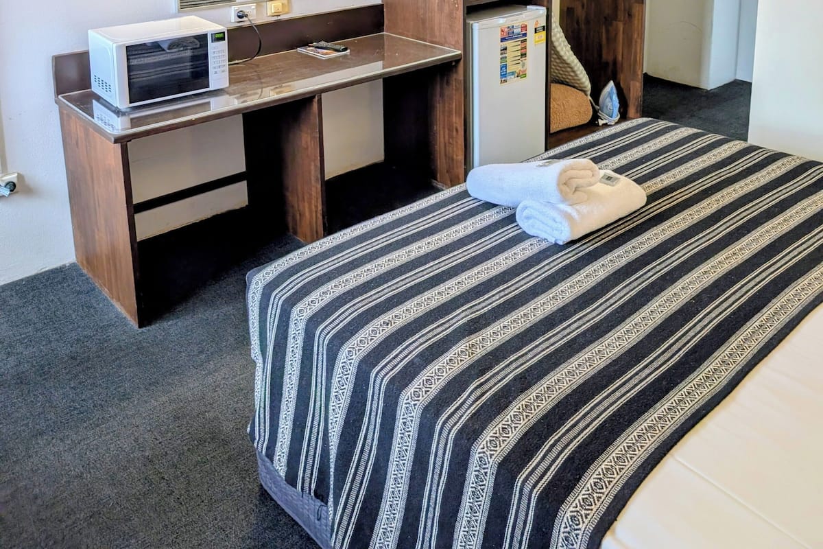A hotel room with a bed, a desk with a microwave, a wardrobe, and a television mounted on the wall.
