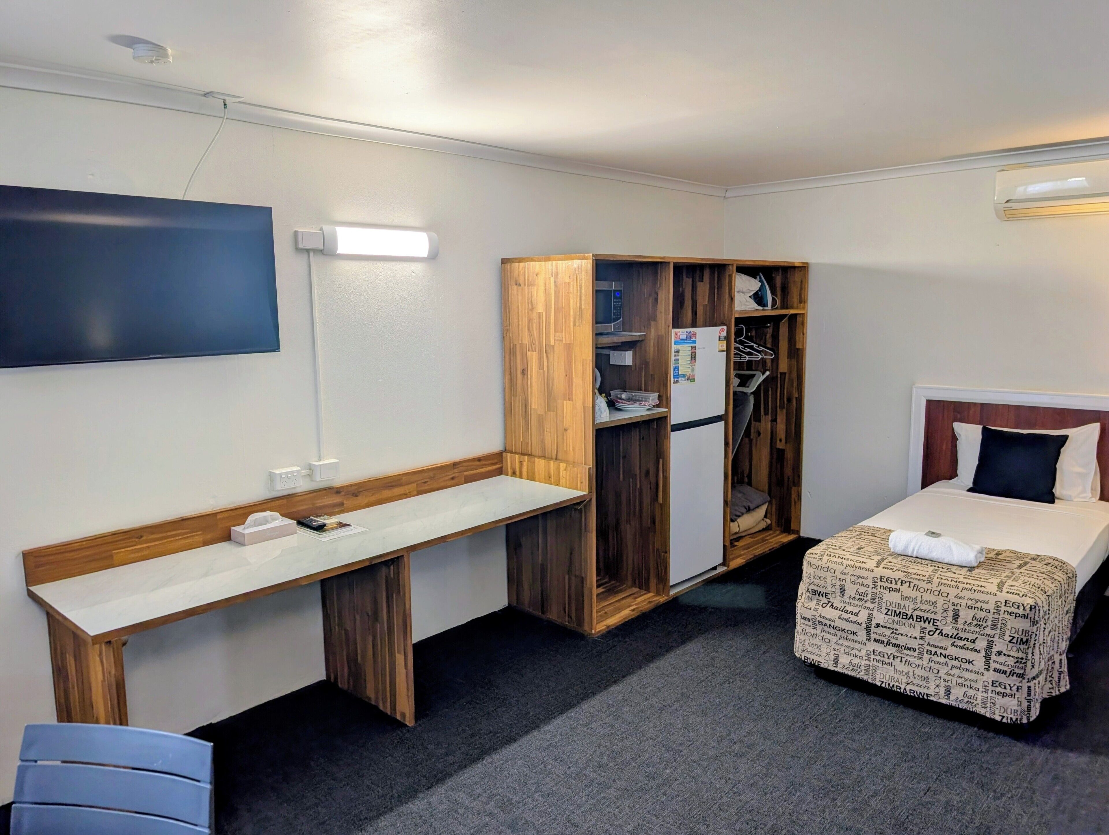 Ett kompakt hotellrum med en säng, ett skrivbord, en garderob och en platt-TV.