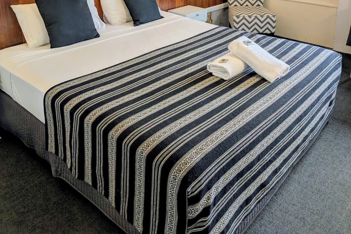 A hotel room with a large bed, a marble-patterned headboard, a wooden nightstand, and a wall-mounted air conditioner.