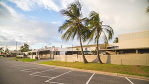 A parking lot with marked spaces, a building with a flat roof, and palm trees. - Hampton Villa Motel (Rockhampton)