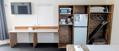 Habitación de hotel compacta con escritorio de madera, microondas, refrigerador, cama con manta estampada y televisor montado en la pared.