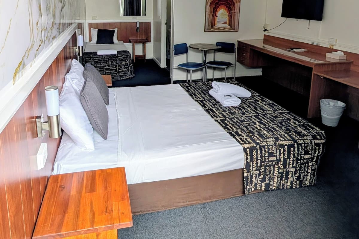 A hotel room with a large bed, a desk, a chair, a TV, and a painting on the wall.