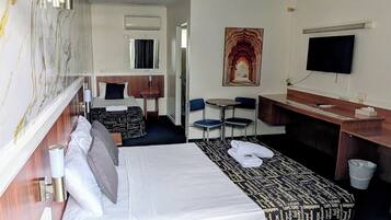 A hotel room with a large bed, a desk, a chair, a TV, and a painting on the wall.