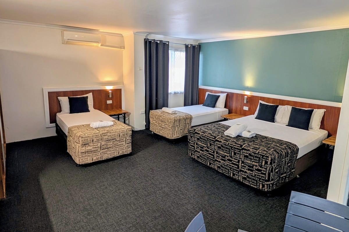 A hotel room with two single beds and a larger bed, all with neatly made linens and pillows.
