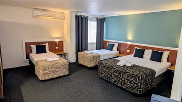 Une chambre d’hôtel avec deux lits simples et un lit plus grand, tous dotés de draps et d’oreillers parfaitement disposés.