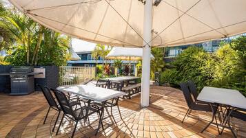 Une terrasse extérieure avec un sol en briques, des tables, des chaises et un grand parasol pour créer de l’ombre.