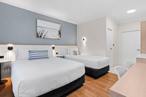Habitación de hotel con dos camas, una mesita de noche, una lámpara, un cuadro en la pared y una puerta.